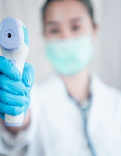 Close-up shot of doctor wearing protective surgical mask ready to use infrared forehead thermometer to check body temperature for virus symptoms